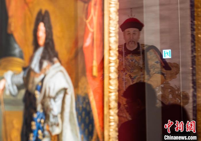 中国侨网2月19日，正在香港故宫文化博物馆持续展出的“当紫禁城遇上凡尔赛宫——十七、十八世纪中法文化交流”展部分珍品焕新亮相，《康熙帝戎装像》《庞巴杜夫人像》等约20件故宫博物院、法国凡尔赛宫的珍贵展品与公众见面，继续“讲述”中法文化之交。图为展厅玻璃映衬的故宫博物院藏《雍正帝朝服像》（右）和法国《路易十四肖像》。中新网记者 侯宇 摄
